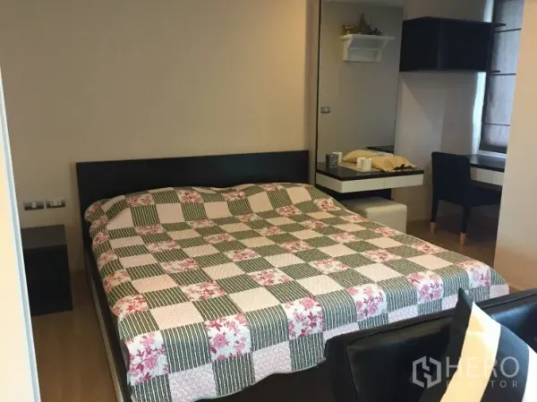 公寓 出租在Watthana, Bangkok - 温馨卧室，双人床搭配花格床品，旁有内置书桌与柔和灯光。