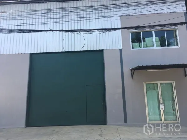 Warehouse for rent in Bang Kapi, Bangkok - Modern warehouse exterior with tall green roller shutter door and a glass-fronted office entry.