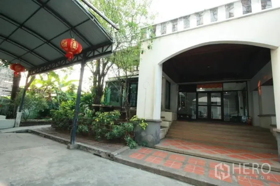 独立式住宅 出租在Bang Phli, Samut Prakan - 房屋前廊拱门入口，陶砖台阶，绿化与有顶停车位。