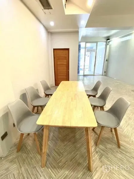 Retail Space for rent in Watthana, Bangkok - Long meeting table with six gray chairs beside the glass entry of a light-filled shop unit.