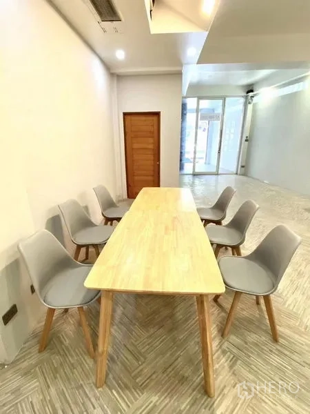 Retail Space for rent in Watthana, Bangkok - Long meeting table with six gray chairs beside the glass entry of a light-filled shop unit.