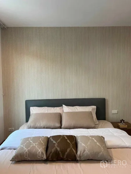 Townhouse for rent in Phra Khanong, Bangkok - Cozy bedroom with striped wallpaper, upholstered headboard and layered pillows on the bed.