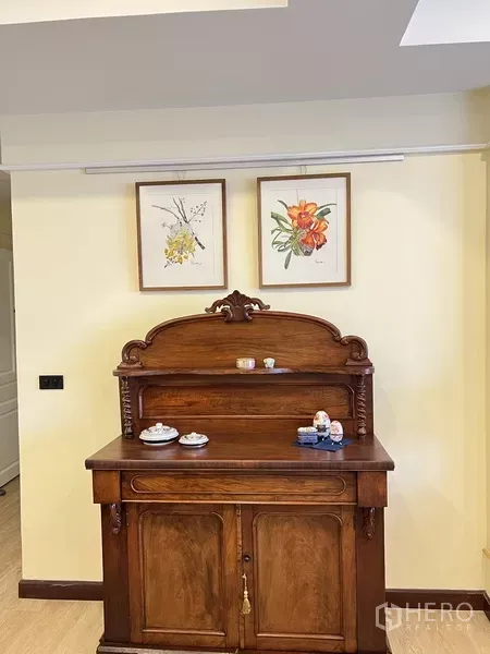 Condominium for rent in Khlong Toei, Bangkok - Close-up of antique wooden sideboard topped with decor beneath botanical wall prints.
