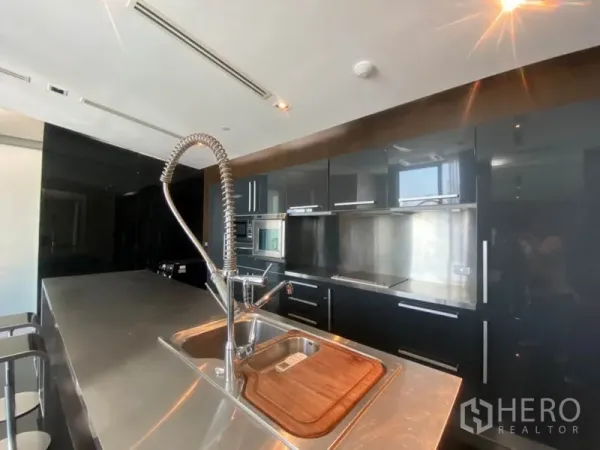Condominium for rent in Sathon, Bangkok - Contemporary kitchen with stainless-steel island sink, pull-down faucet and glossy black cabinetry with built-in appliances.