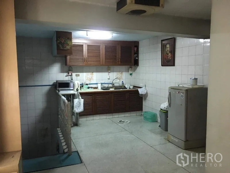 Shophouse for rent in Phra Khanong, Bangkok - Tiled kitchen with wooden cabinets, sink, microwave, and refrigerator.