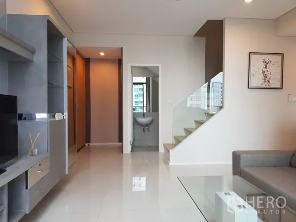 公寓 出租在Ratchathewi, Bangkok - 客厅视角带电视柜、玻璃栏杆楼梯及通往盥洗区的门。