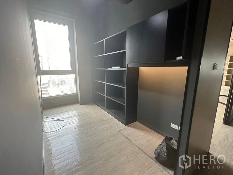 Office Space for rent in Bang Rak, Bangkok - Compact private office with built-in black shelving and a window facing the city skyline.