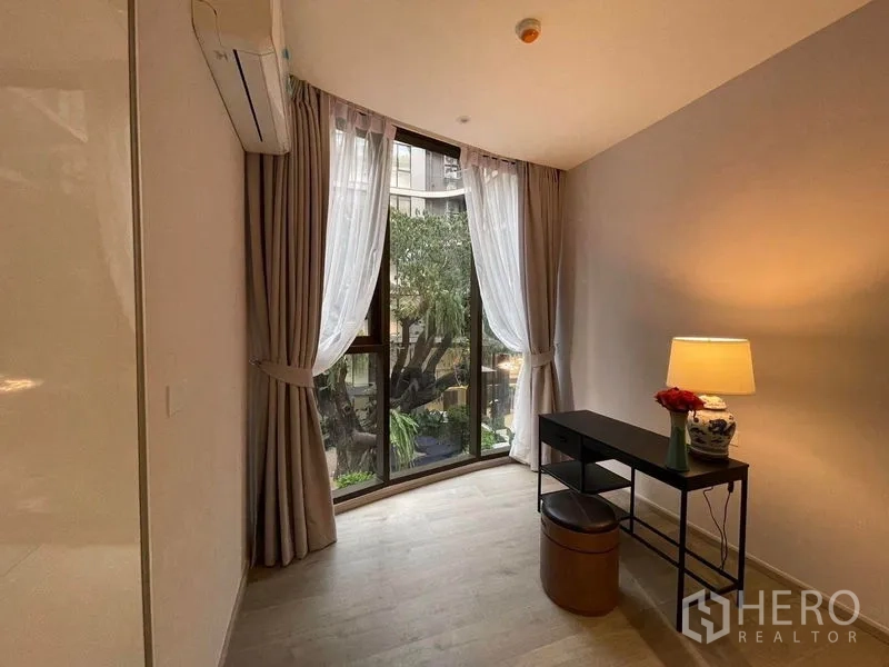 Condominium for rent in Khlong Toei, Bangkok - Bedroom or study with desk, lamp and floor-to-ceiling window facing courtyard tree