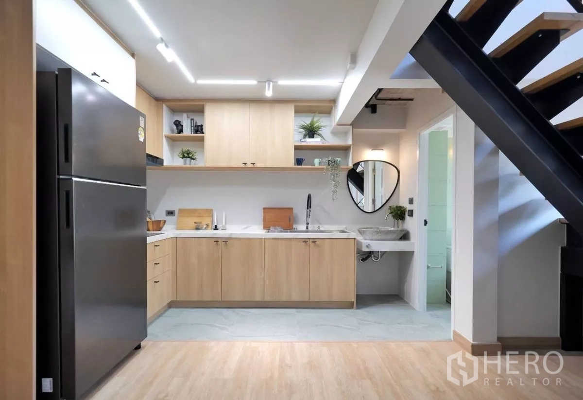 Townhouse for rent in Watthana, Bangkok - Full kitchen view beneath the stairs with open shelving, sink and ample countertop next to a bathroom door.