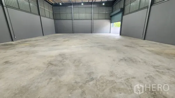 Factory for rent in Bang Bo, Samut Prakan - Spacious warehouse with an open roller door to the loading yard and LED lighting overhead.