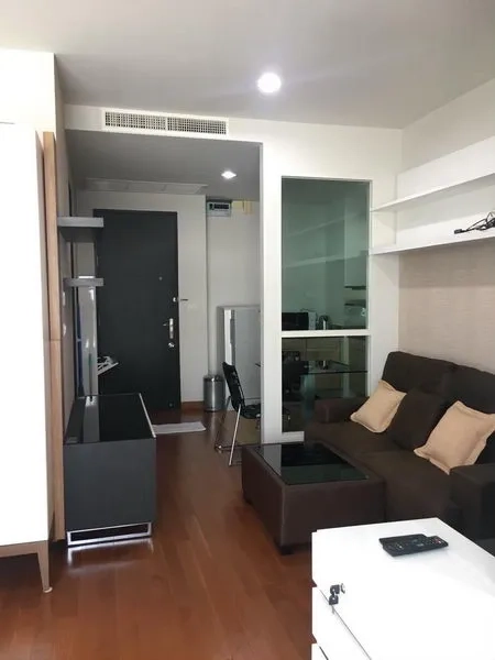 公寓 出租在Pathum Wan, Bangkok - 入口与客厅一体化布局，棕色沙发、置物架与木地板。