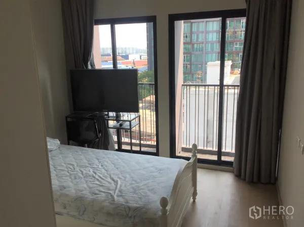 Condominium for rent or sale in Watthana, Bangkok - Cozy bedroom with balcony doors, city view, TV stand and blackout curtains.