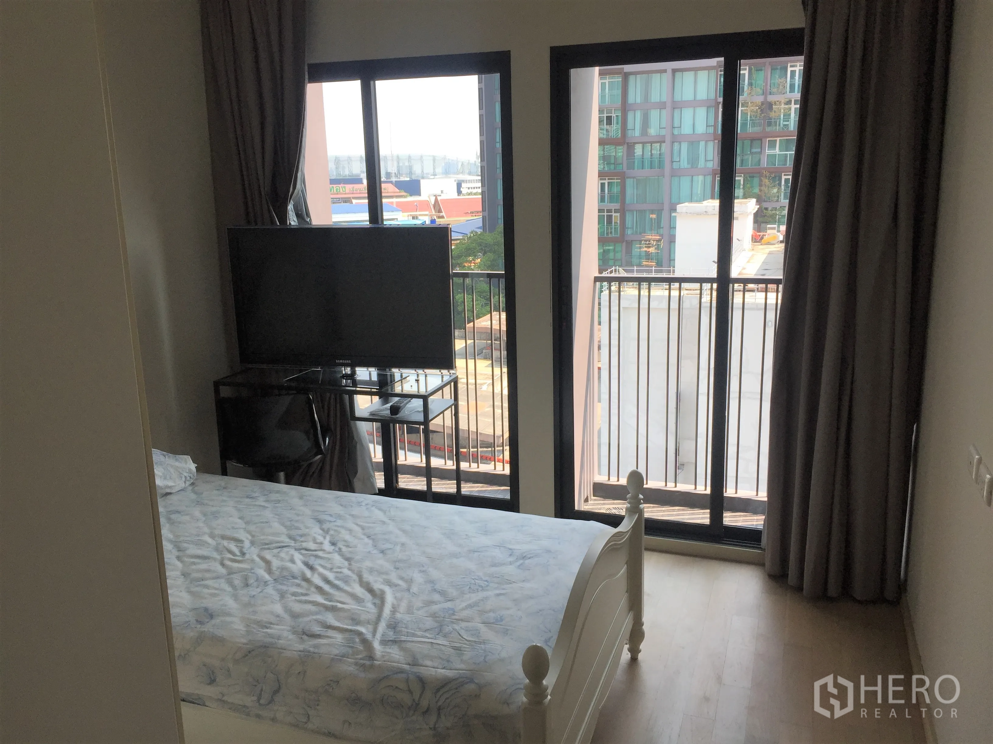 Condominium for rent or sale in Watthana, Bangkok - Cozy bedroom with balcony doors, city view, TV stand and blackout curtains.