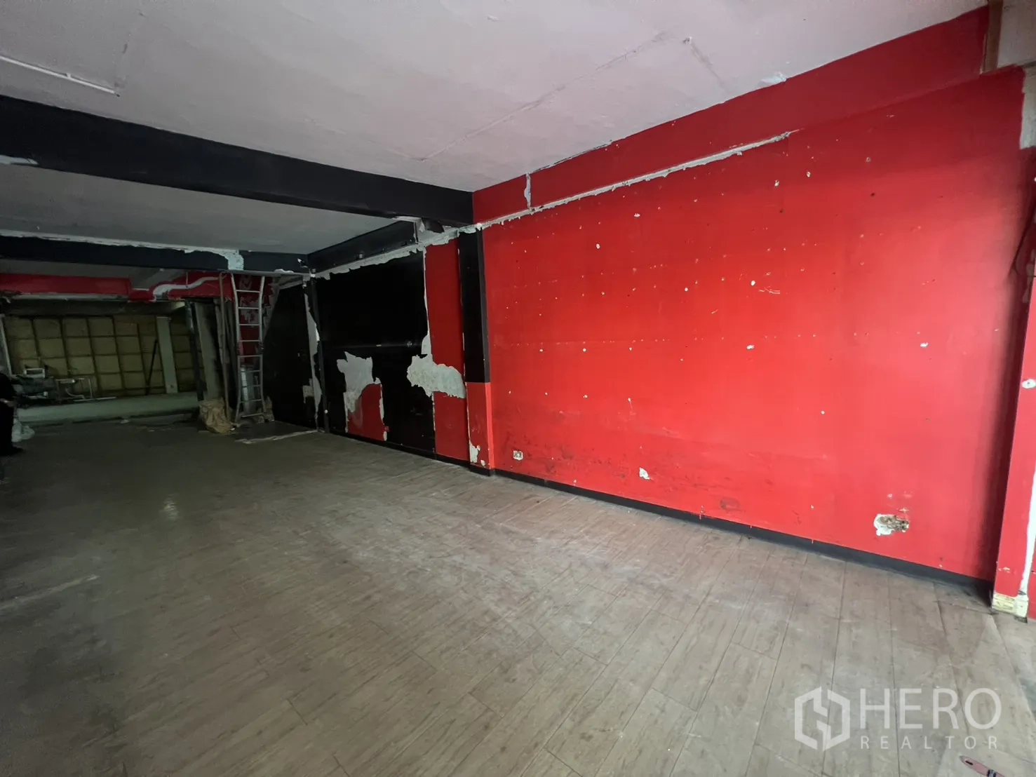Shophouse for rent in Khlong Toei, Bangkok - Wide open-plan retail space with red accent wall and exposed beams, ready for renovation.