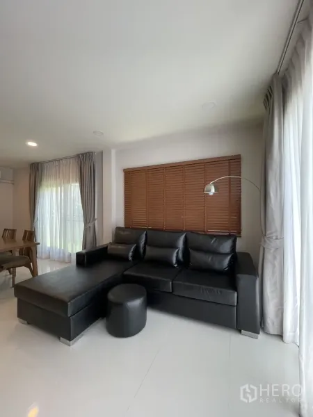 独立式住宅 出租在Bang Phli, Samut Prakan - 黑色L型皮沙发，窗边百叶与落地灯。