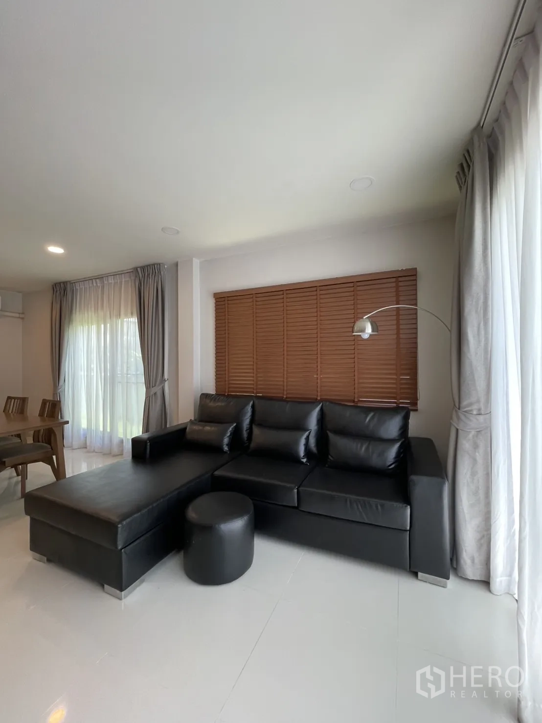 独立式住宅 出租在Bang Phli, Samut Prakan - 黑色L型皮沙发，窗边百叶与落地灯。
