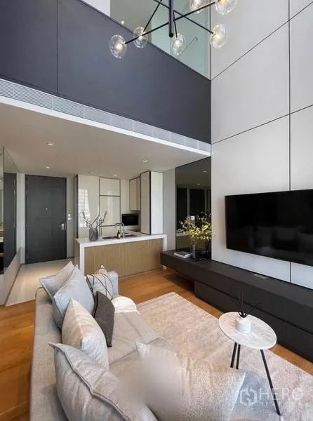 Condominium for rent in Khlong Toei, Bangkok - Living area beneath a mezzanine with TV console, sofa and open kitchen layout.