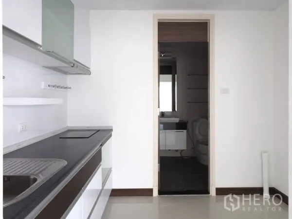 公寓 出租在Yan Nawa, Bangkok - 极简白色厨房，内置灶台、水槽与橱柜，连通浴室。