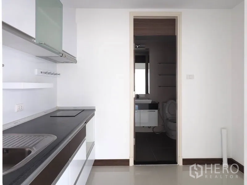 公寓 出租在Yan Nawa, Bangkok - 极简白色厨房，内置灶台、水槽与橱柜，连通浴室。
