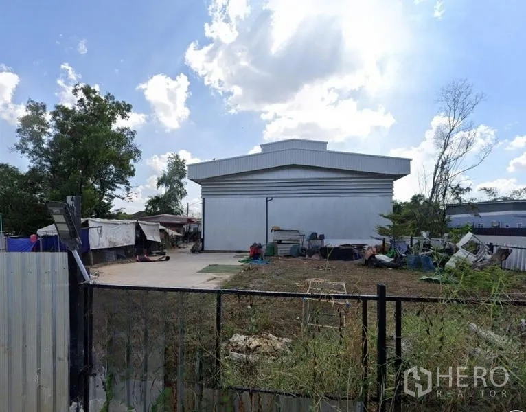 货栈 出售在Mueang Nonthaburi, Nonthaburi - 大门外观视角，银色仓库与开放堆场，蓝天白云。
