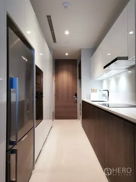 公寓 出租或出售在Watthana, Bangkok - 走廊式现代厨房，白色橱柜、内嵌电器与不锈钢冰箱。