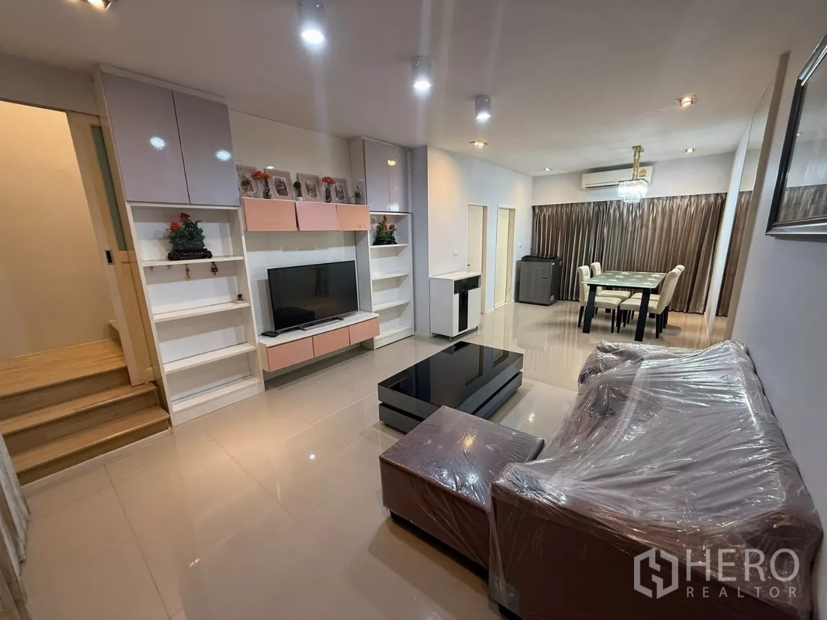 Townhouse for rent in Suan Luang, Bangkok - Open-plan living and dining area with built-in TV wall, glossy floors and sofa set.