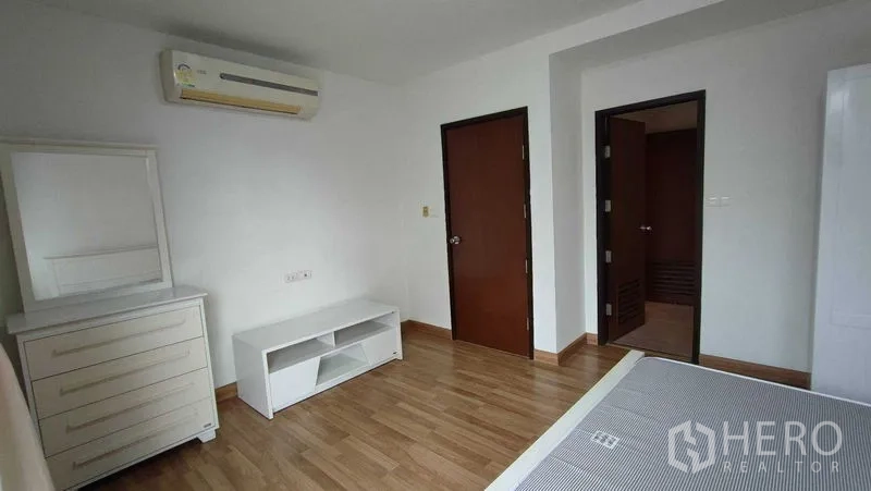 Condominium for rent in Khlong Toei, Bangkok - Bedroom corner with dresser, TV console, air conditioner and two doors on wood flooring.