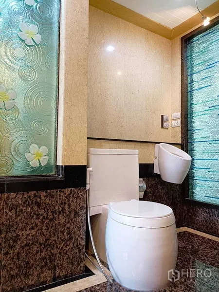 公寓 出租在Watthana, Bangkok - 现代卫生间，白色坐便器，石材质感墙地面与纹理磨砂玻璃窗。