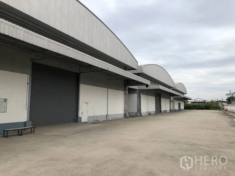 货栈 出租在Bang Phli, Samut Prakan - 仓库外立面，多个带雨棚的装卸月台、卷闸门与宽阔混凝土场地，适合卡车停靠，位于邦普里北榄府。