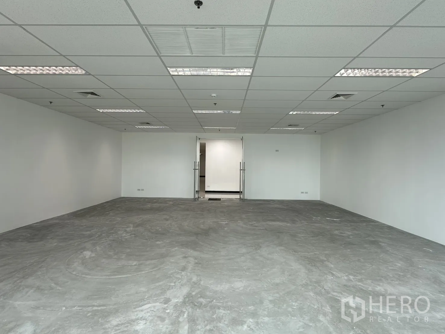 办公室 for rent in Watthana, Bangkok - 面向双扇玻璃门的开放式办公空间，顶置照明与混凝土地面。