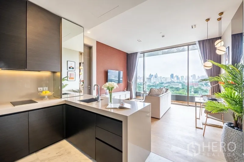 Condominium for rent or sale in Bang Rak, Bangkok - Open-plan kitchen with black cabinetry and white island facing a bright living room and floor-to-ceiling windows with city and park views.