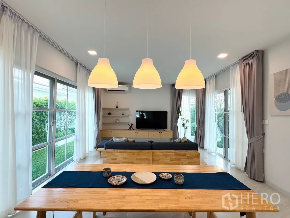 独立式住宅 出租在Bang Phli, Samut Prakan - 三盏吊灯位于木质餐桌上方，面向花园与客厅