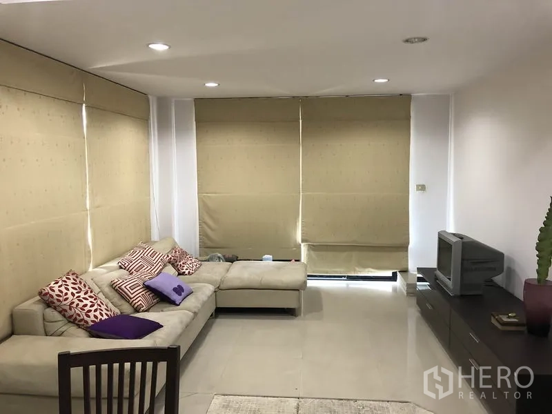 带办公室的家 出租在Wang Thonglang, Bangkok - 客厅配L型沙发、电视柜、瓷砖地面及大幅卷帘。