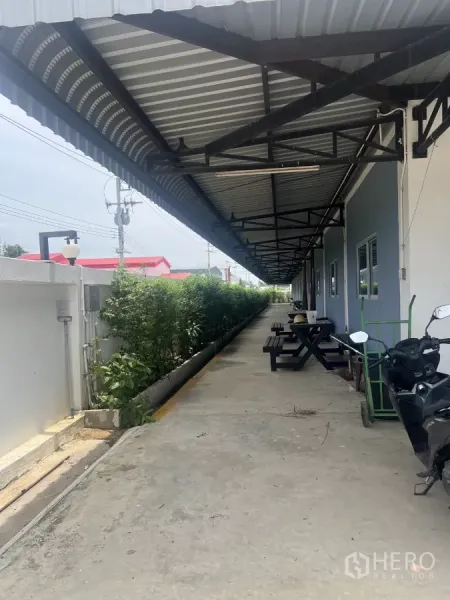 Factory for sale in Lat Lum Kaeo, Pathum Thani - Covered walkway with metal awning, benches, and landscaped greenery beside the building.