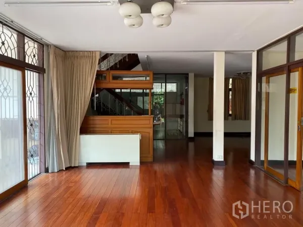 独立式住宅 出租在Khlong Toei, Bangkok - 客厅明亮，实木地板，大窗配防盗格栅，并设楼梯通往二层。