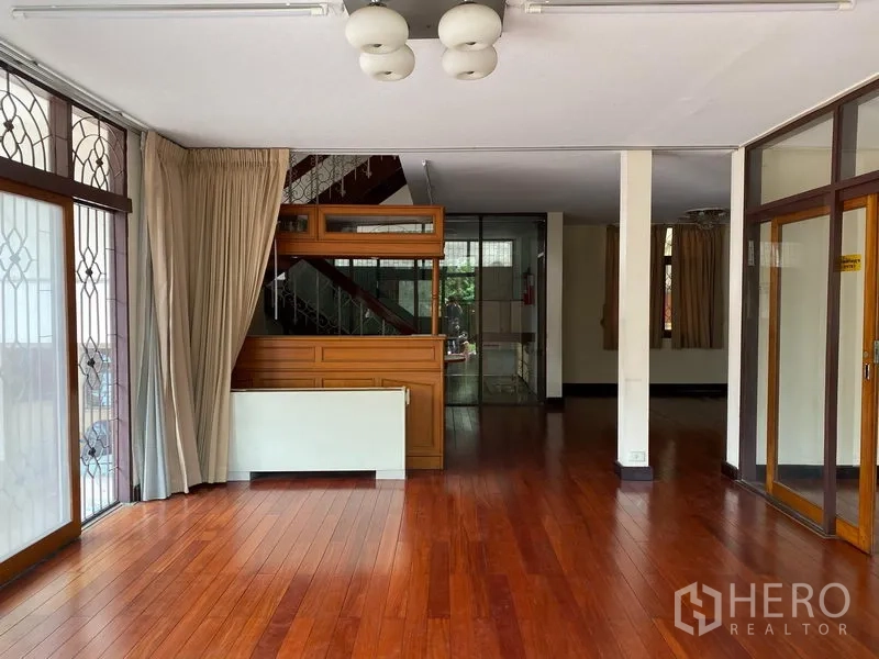 独立式住宅 出租在Khlong Toei, Bangkok - 客厅明亮，实木地板，大窗配防盗格栅，并设楼梯通往二层。
