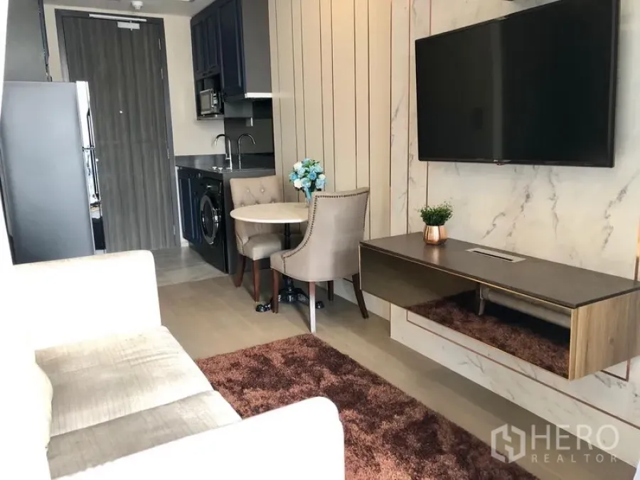 公寓 出租在Watthana, Bangkok - 一体化客厅与小厨房，配沙发、壁挂电视和小餐桌