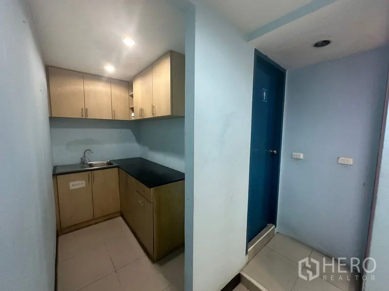 Office Space for sale - Pantry with upper and lower cabinets, sink and adjacent restroom door.