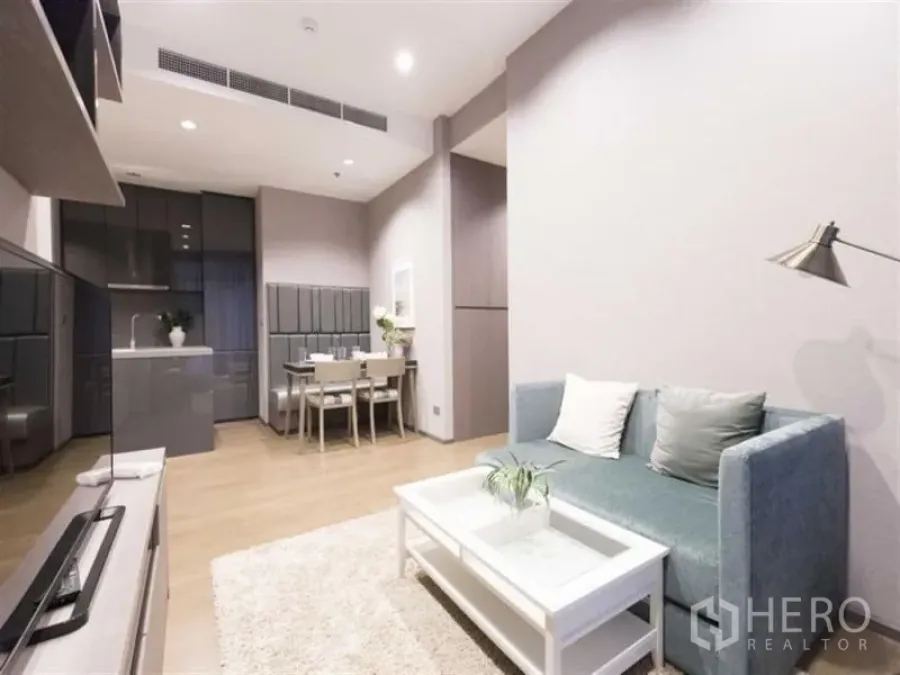 公寓 出租在Bang Rak, Bangkok - 明亮的开放式客厅，青绿色沙发与白色茶几，连通餐区与灰色橱柜厨房，浅木地板。