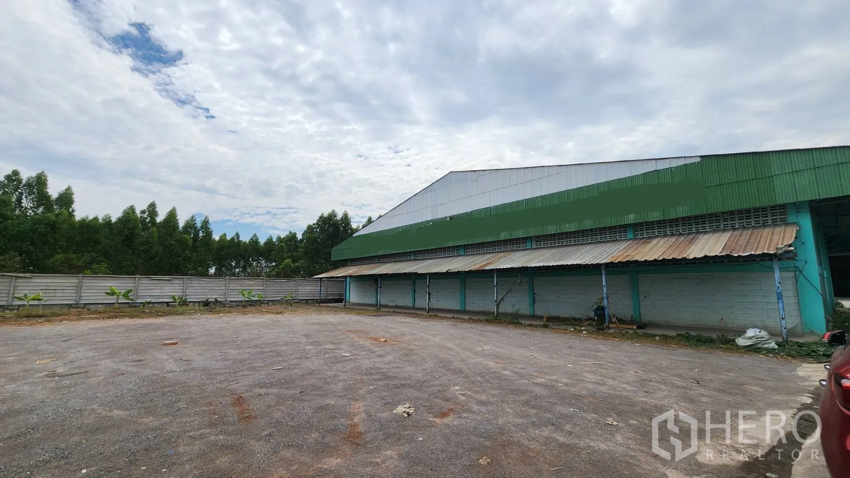 Warehouse for rent in Krathum Baen, Samut Sakhon - Side yard beside the warehouse with a perimeter fence, trees, and a covered loading dock.