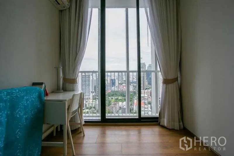 Condominium for sale in Khlong Toei, Bangkok - Secondary bedroom or study with desk and tall window overlooking the skyline.