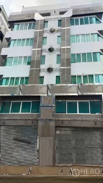 Office Space for rent in Prawet, Bangkok - Facade of a mid-rise office building with green-tinted windows and metal roller shutters in Prawet, Bangkok.