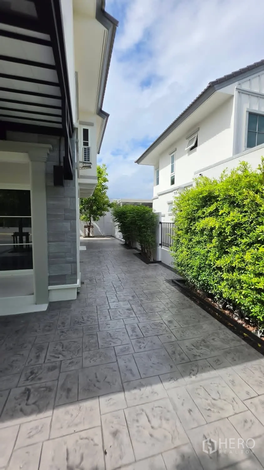 独栋房屋 for rent in Bang Phli, Samut Prakan - 侧院灰色地砖、绿篱及邻近的现代住宅。