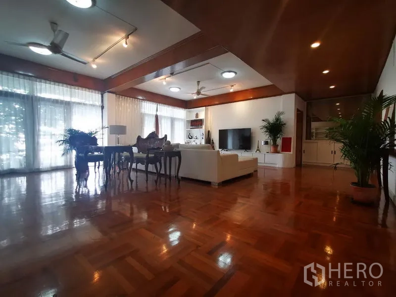Apartment for rent in Khlong Toei, Bangkok - Open-plan lounge and dining area with floor-to-ceiling windows, TV wall and glossy hardwood flooring.