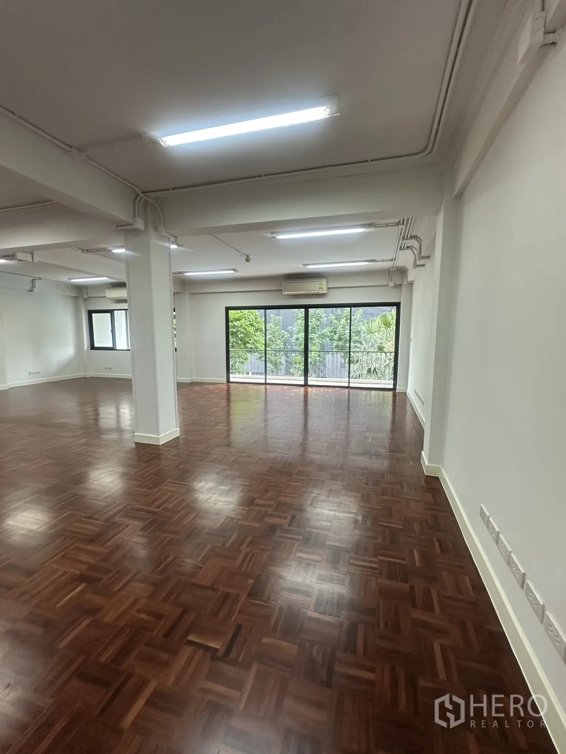 Office Space for rent in Watthana, Bangkok - Open-plan office with polished parquet flooring and large sliding glass doors to a balcony.