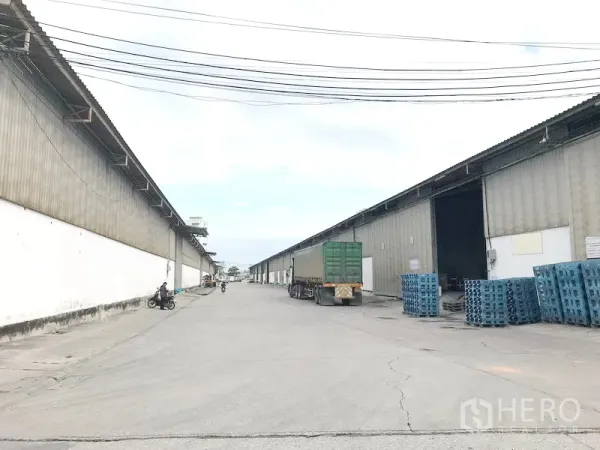 Warehouse for rent in Bang Sao Thong, Samut Prakan - Wide driveway between large corrugated warehouses with loading bays and trucks in Bang Sao Thong.