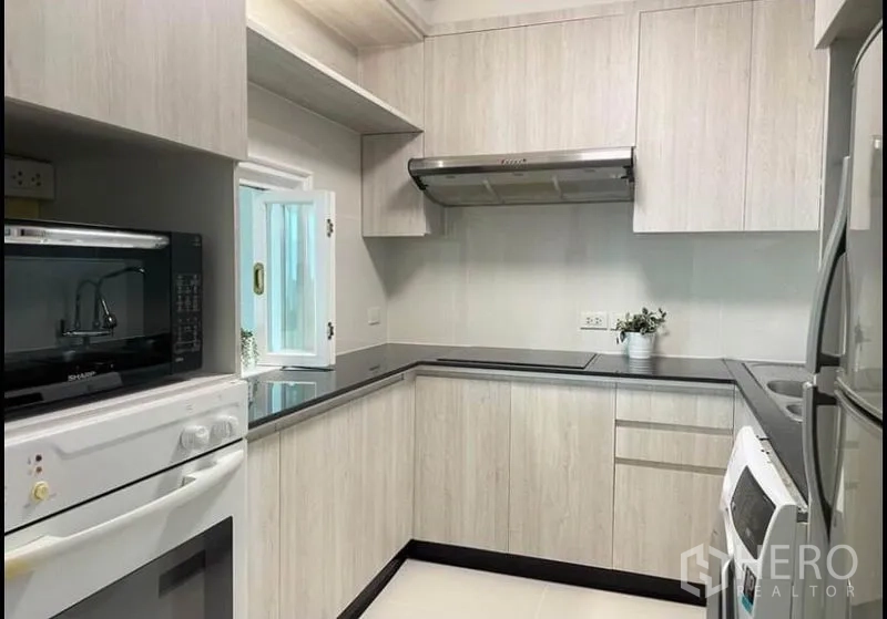 Condominium for rent in Sathon, Bangkok - L-shaped kitchen with light wood cabinets, range hood, oven and refrigerator.