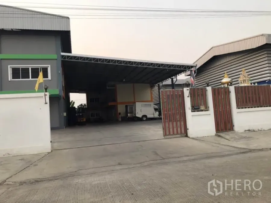 Factory for sale in Pak Kret, Nonthaburi - Gated factory exterior with wide concrete yard and a large covered loading bay.