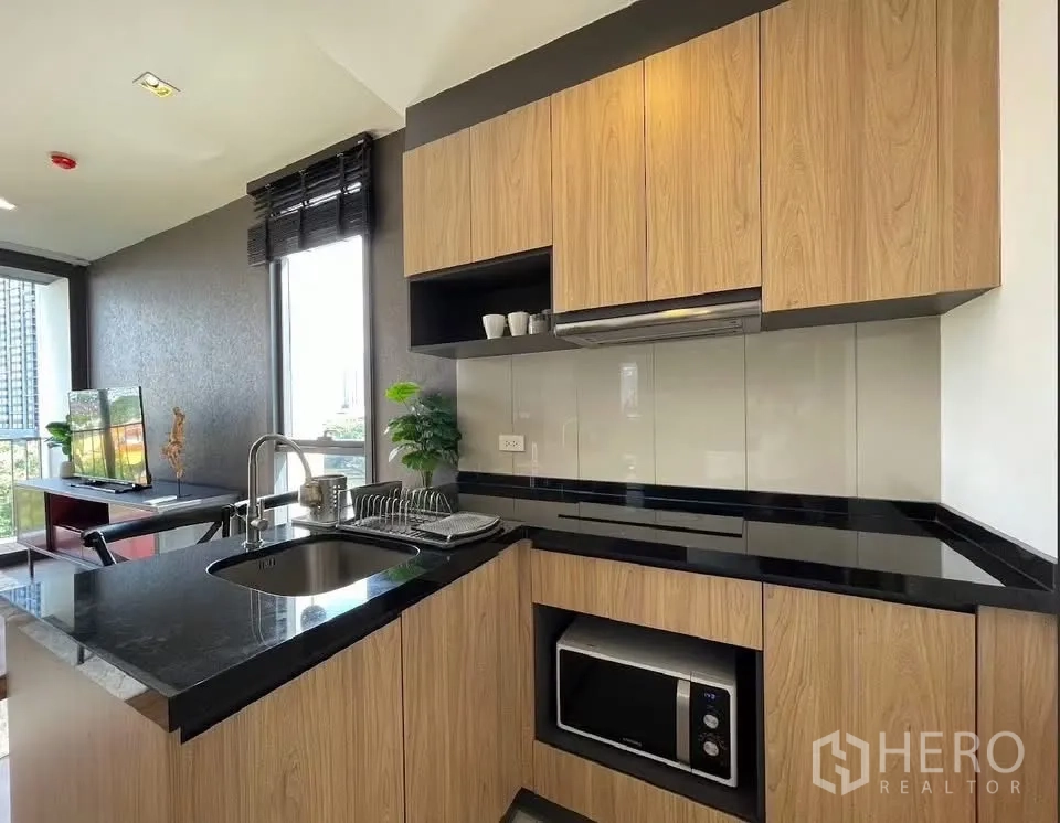 Condominium for rent in Watthana, Bangkok - Close-up of modern kitchen with sink, microwave, and open shelving beside the living area.