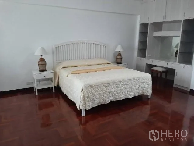 公寓 出租在Khlong Toei, Bangkok - 宽敞主卧，白色床头配床头灯，内置衣柜与梳妆台，实木地板光亮整洁。